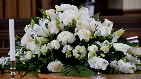 White funeral flowers on top of dark wood coffin in chapel
