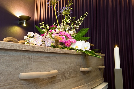 Wooden casket with colourful flower arrangement with light in the background