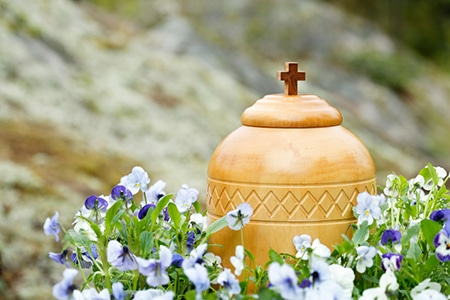 Wood urn with cross on lid surrounded by white and purple flowers in Darwin