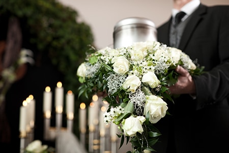 Silver urn carried by man in suit with white flowers in a Darwin chapel