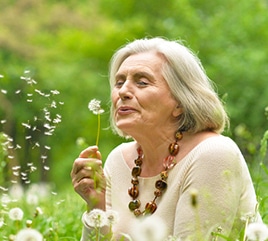 Old lady blowing on dandelion flower sitting on grass in Darwin