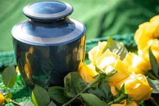 Black glossy urn on grass with yellow flowers